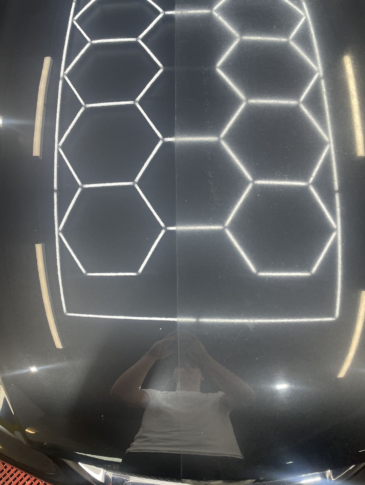 Black bonnet reflecting hexagon lights after paint correction